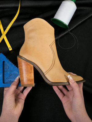 A handmade leather boot is held, surrounded by sewing tools. Ideal for fashion and craft themes.